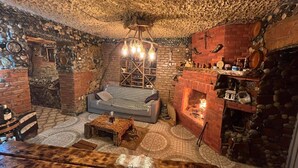A cozy, rustic room with a stone wall, a brick fireplace, a wooden sofa, and a hanging light fixture.