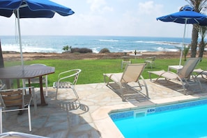 A pool area with a view of the ocean, outdoor seating, and a stone patio.