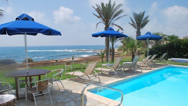 Zona de piscina con sillones, sombrillas y vista al océano.