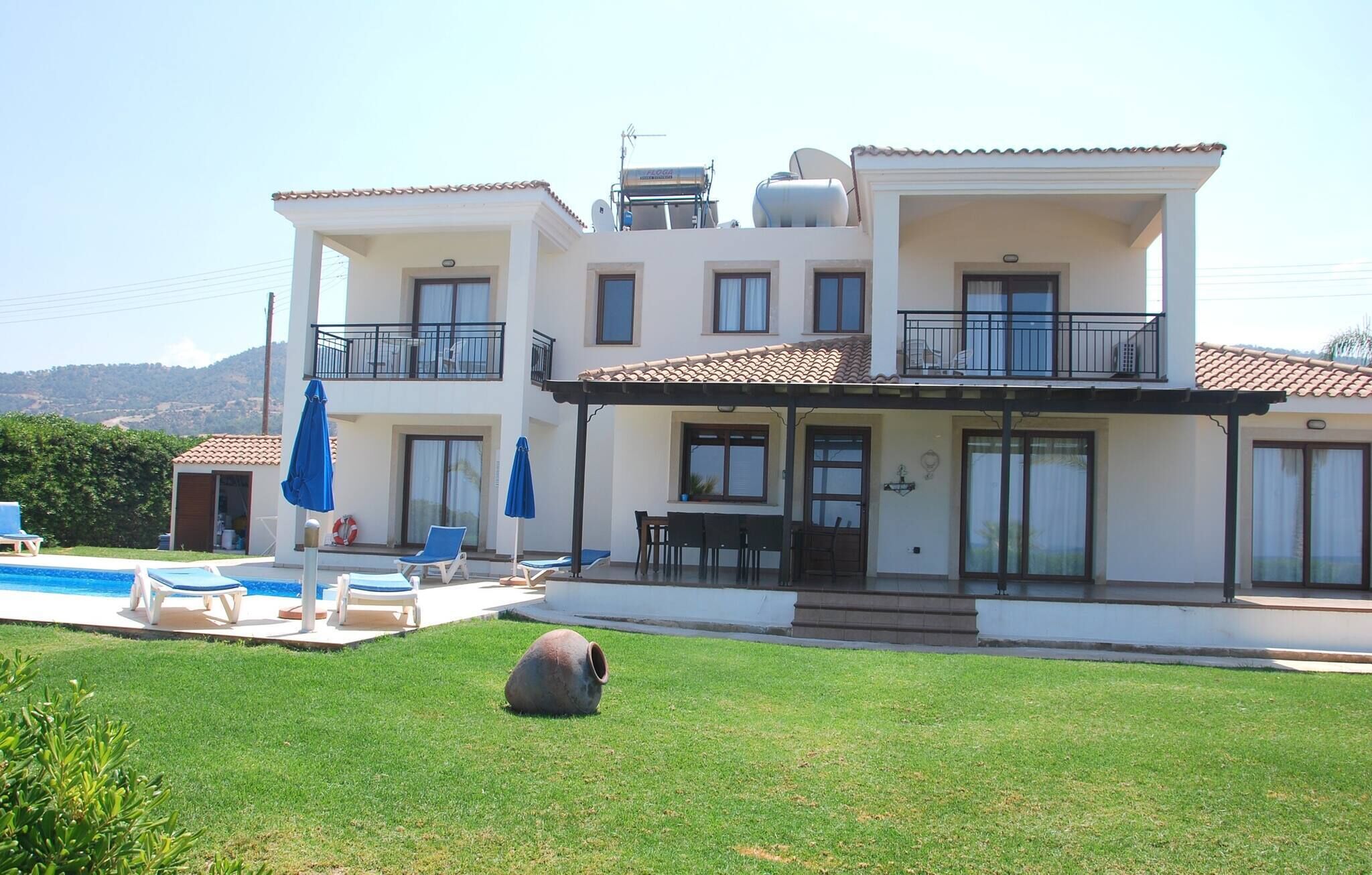 A two-story house with a swimming pool, outdoor seating, and a large rock in the yard.