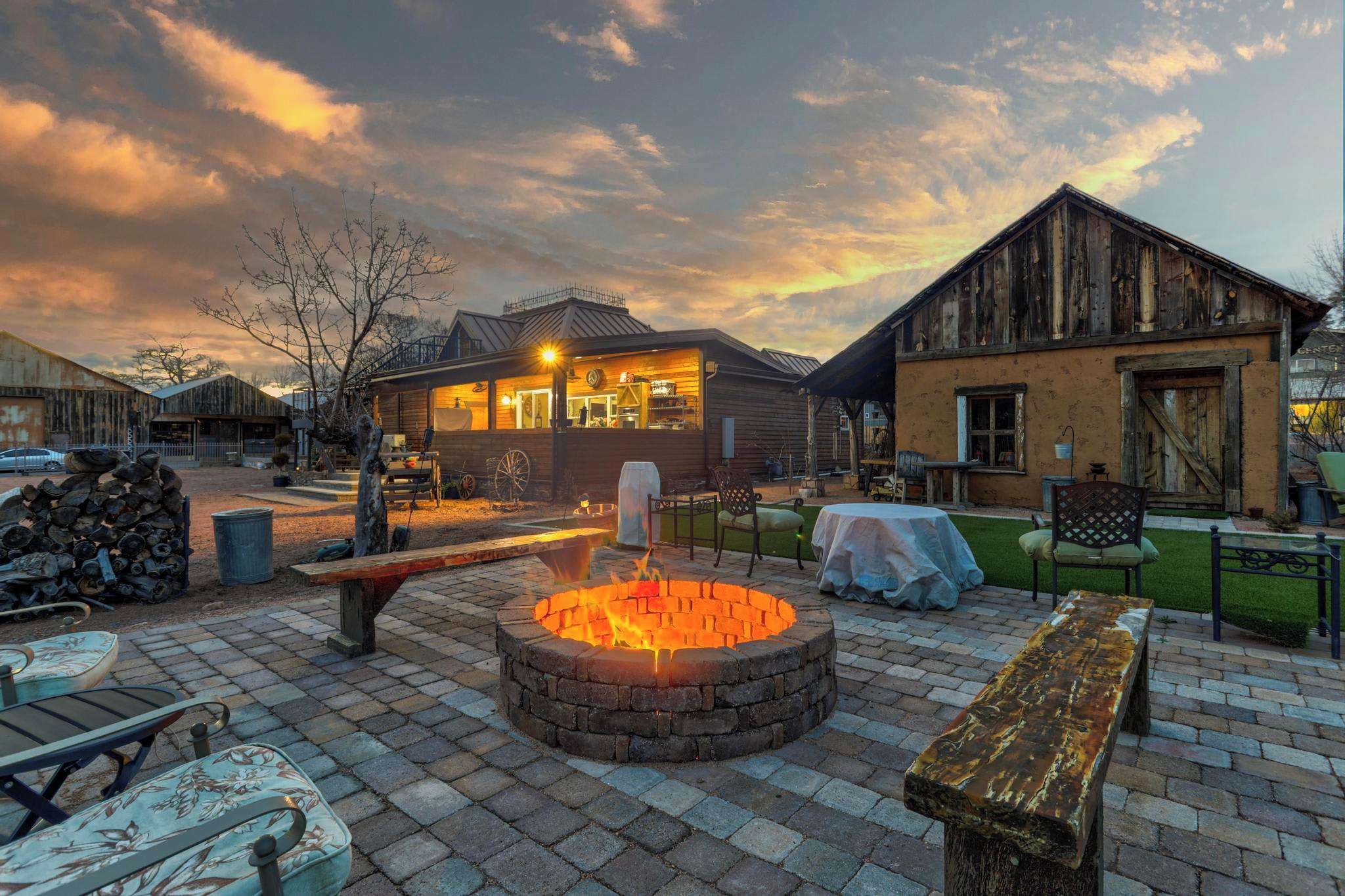 A rustic outdoor seating area with a fire pit, wooden benches, and a brick patio.