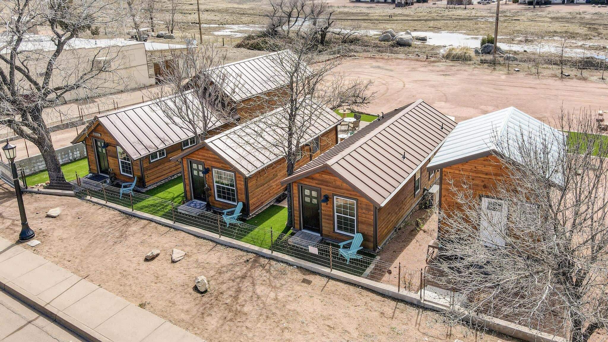 A row of wooden cabins with metal roofs, each with a porch and a small garden area.