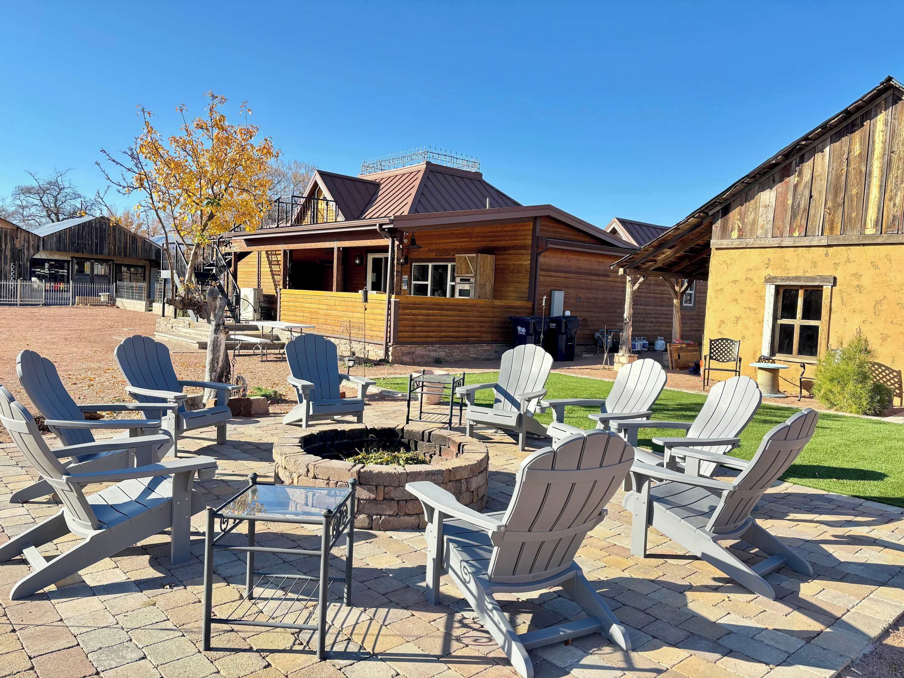 A patio area with Adirondack chairs and a fire pit, surrounded by wooden cabins with a covered porch.