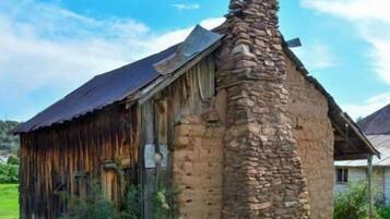 A rustic stone building with a steeply pitched roof and a chimney.