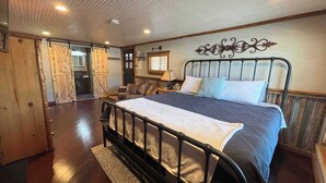 Une chambre avec un grand lit, un plancher en bois, une tête de lit décorative et une fenêtre avec des stores.