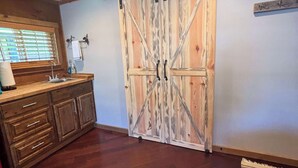 Une cuisine rustique avec des meubles en bois, une porte coulissante de style champêtre et une fenêtre avec des stores.