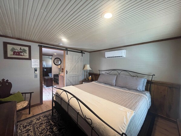 A bedroom with a bed, bedside table, lamp, and an air conditioning unit. - Mini Cabin with Pickle ball court ! (Payson)