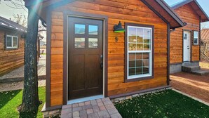 En hyggelig træhytte med en mørkebrun dør, et vindue med hvid ramme og en lille veranda.