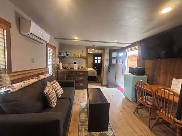 A compact living space with a sofa, a coffee table, a dining table with chairs, a kitchenette, and a TV. - Mini Cabin with Pickle ball court ! (Payson)