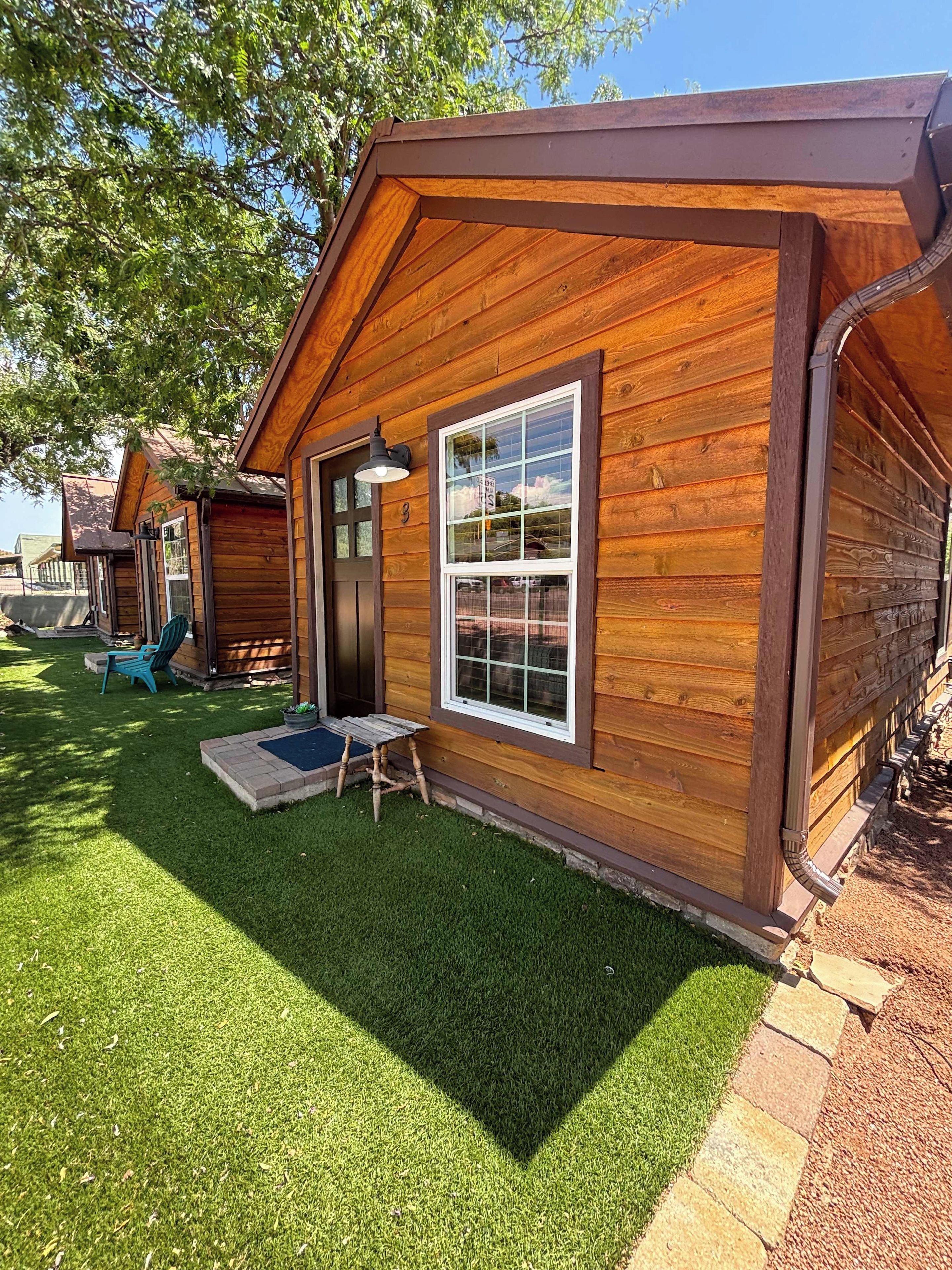 A wooden cabin with a front door, a window, and a small porch area with a bench and a potted plant.