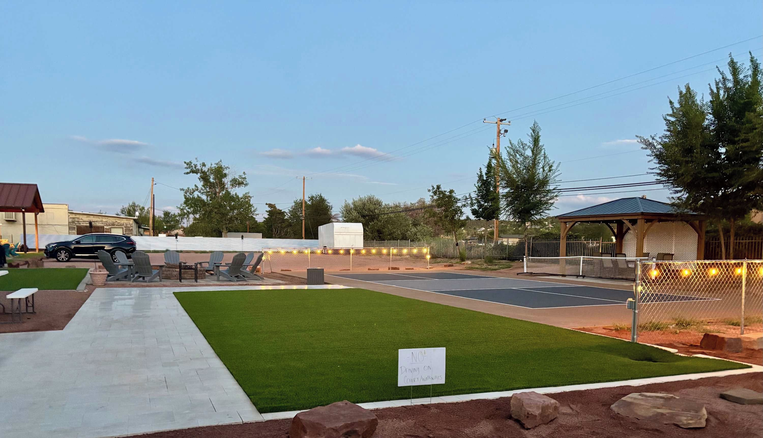 A well-maintained outdoor area with a paved walkway, green lawn, and a fenced tennis court.