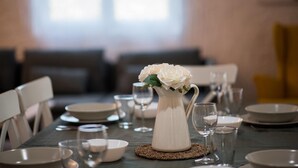 A dining table set with white plates, bowls, and wine glasses, centered with a white vase containing white flowers.