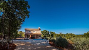 A two-story stone house with a tiled roof, a swimming pool, and a gravel driveway.