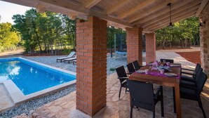 A covered patio with a pool, outdoor seating, and a brick column structure.