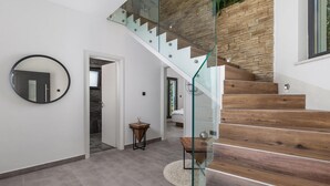A modern interior with a wooden staircase, a round mirror, and a glass railing.