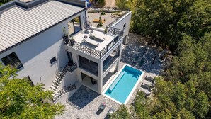 A modern two-story building with a rooftop terrace, a swimming pool, and a garden area.