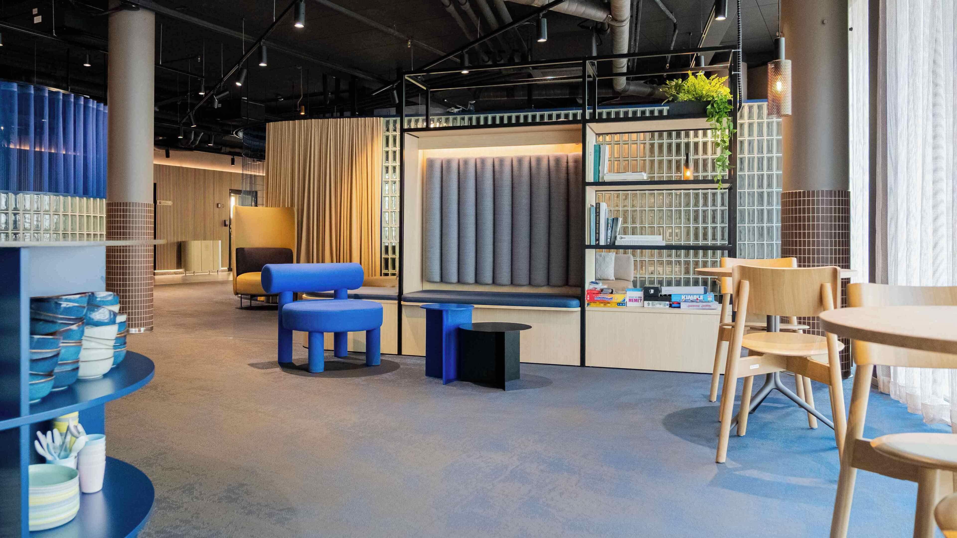 A modern lounge area with seating, a bookshelf, and a plant.