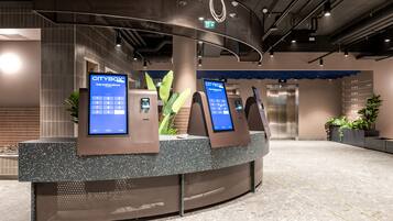 A modern reception area with a curved counter, two digital kiosks, and an elevator in the background.