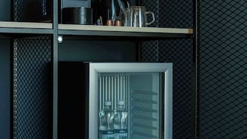 Uma geladeira compacta com porta transparente, contendo duas garrafas de água e uma máquina de café na prateleira superior.