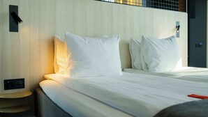 Una habitación de hotel con una cama bien hecha, una mesita de noche y una lámpara fijada en la pared.