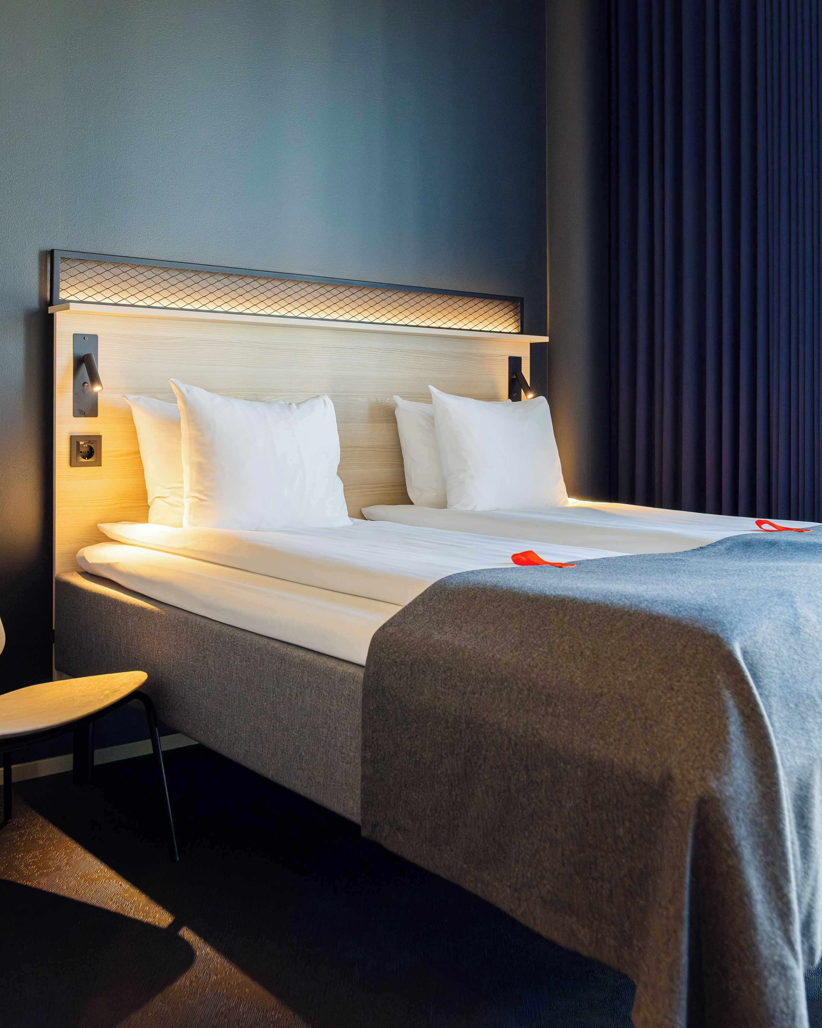 A neatly made bed with white linens and pillows, a bedside table, and a wall-mounted light fixture.