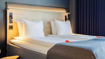 A neatly made bed with white linens and pillows, a bedside table, and a wall-mounted light fixture.