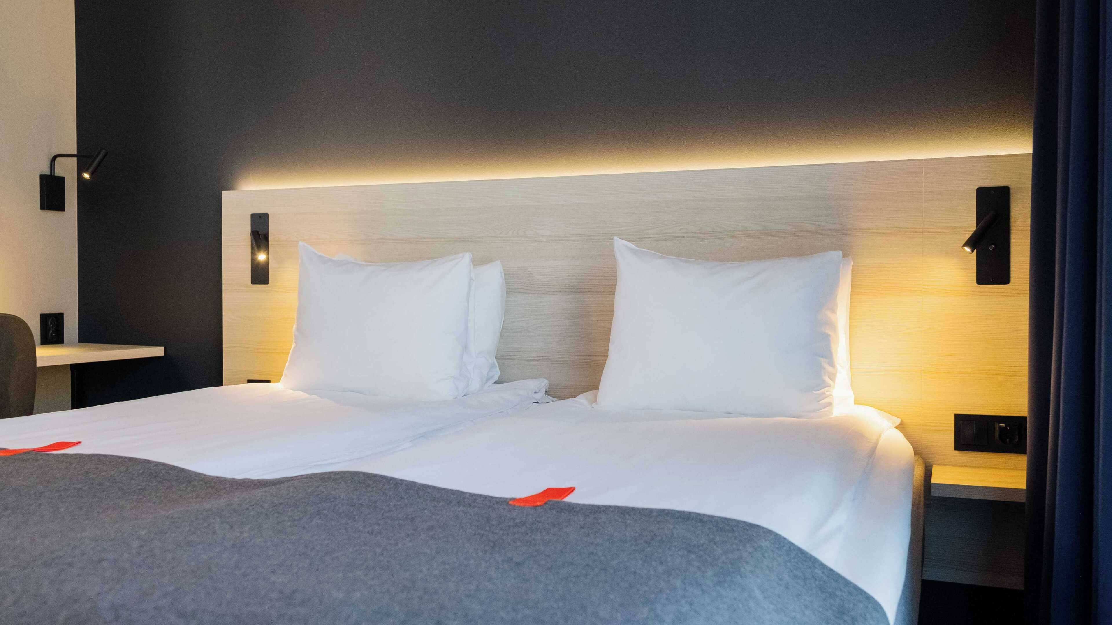 Une chambre d’hôtel avec un grand lit, deux tables de chevet et une tête de lit moderne.