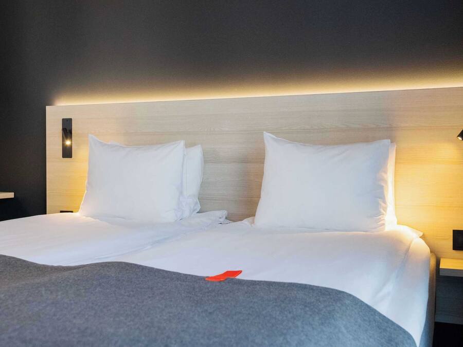 Une chambre d’hôtel avec un grand lit, deux tables de chevet et une tête de lit moderne.