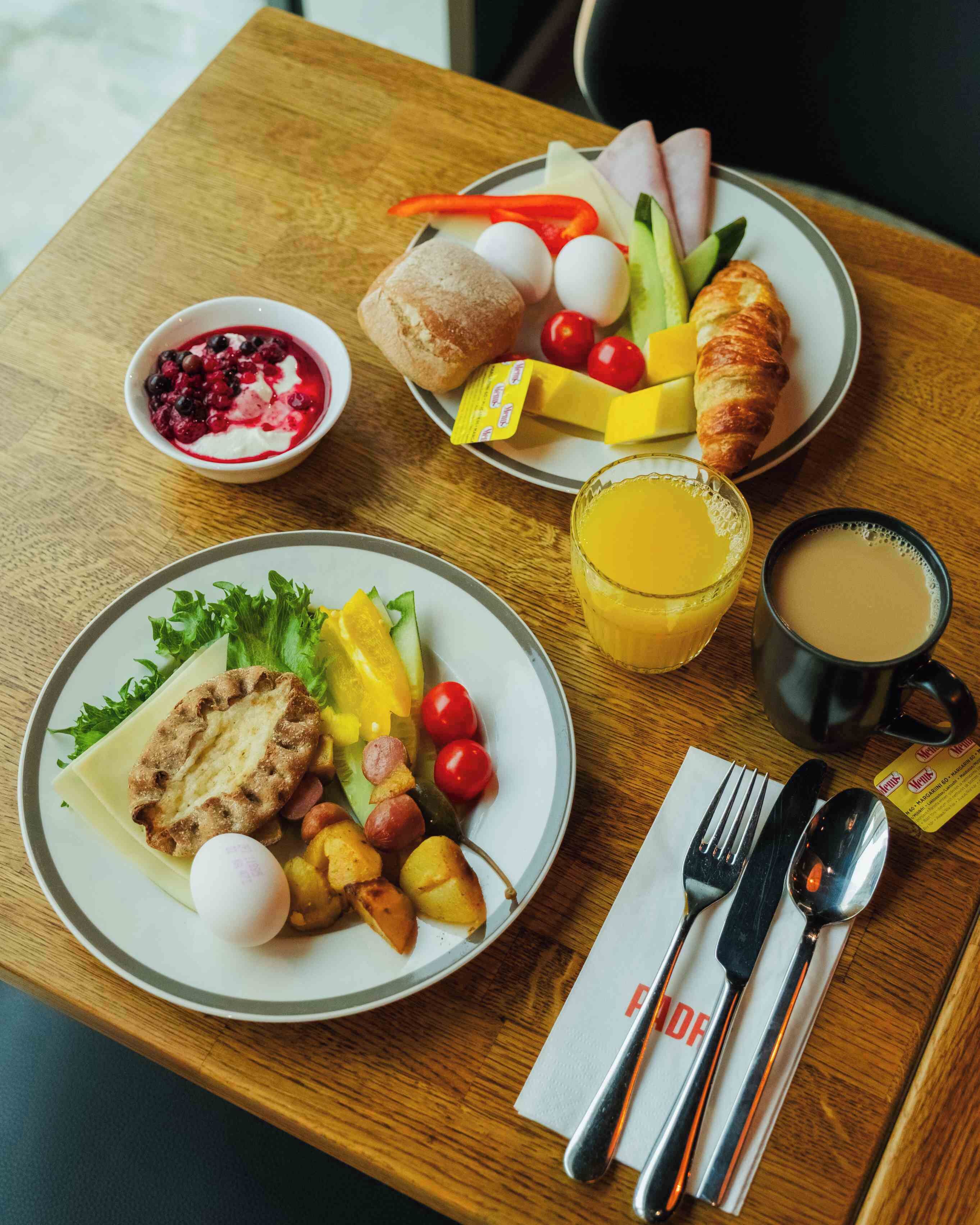 A breakfast tray with croissants, eggs, tomatoes, cucumbers, and a bowl of berries.