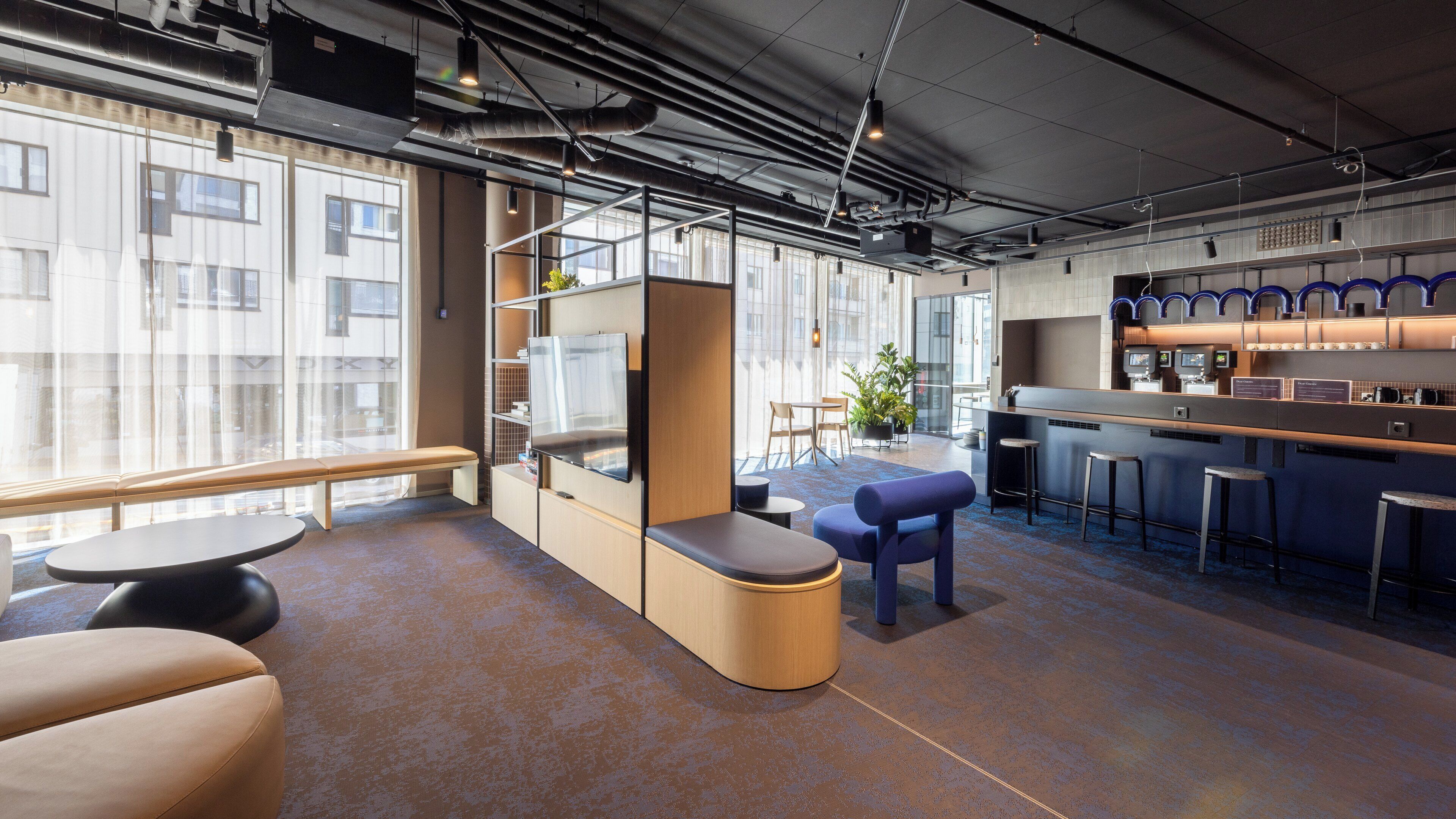 A modern office space with a bar area, seating, and large windows.