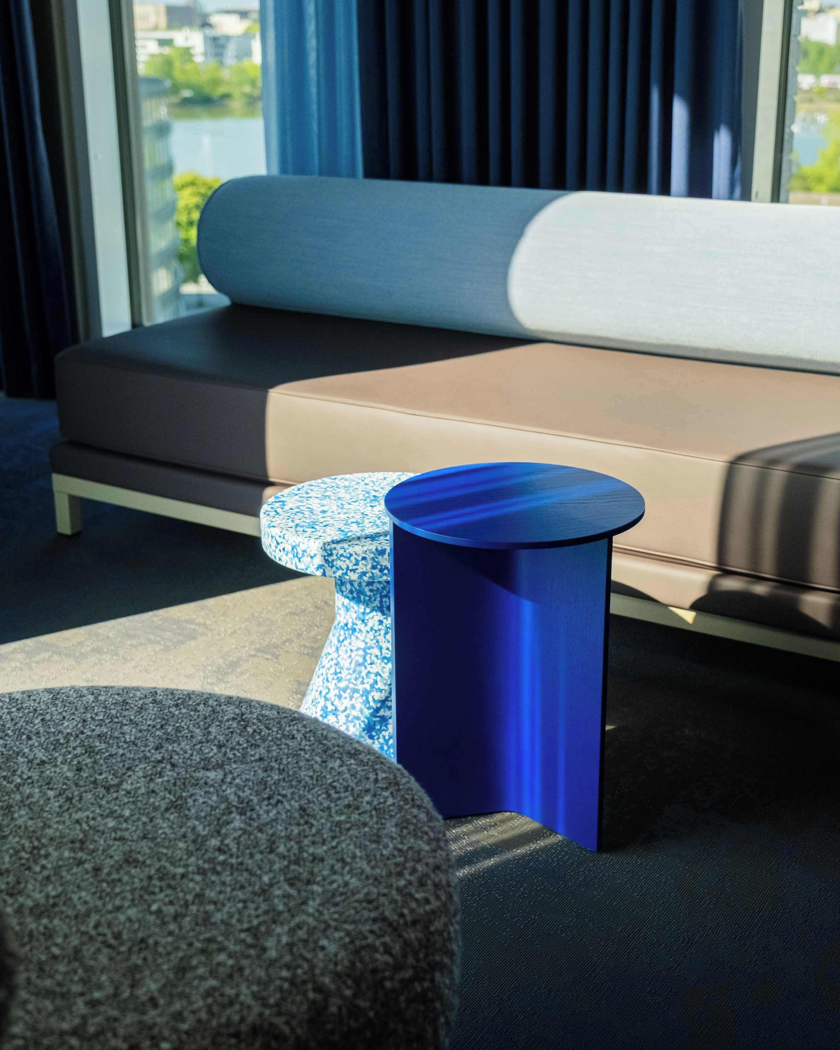 Een moderne woonkamer met een bank, een blauwe cilindrische bijzettafel en een gestreept hocker.