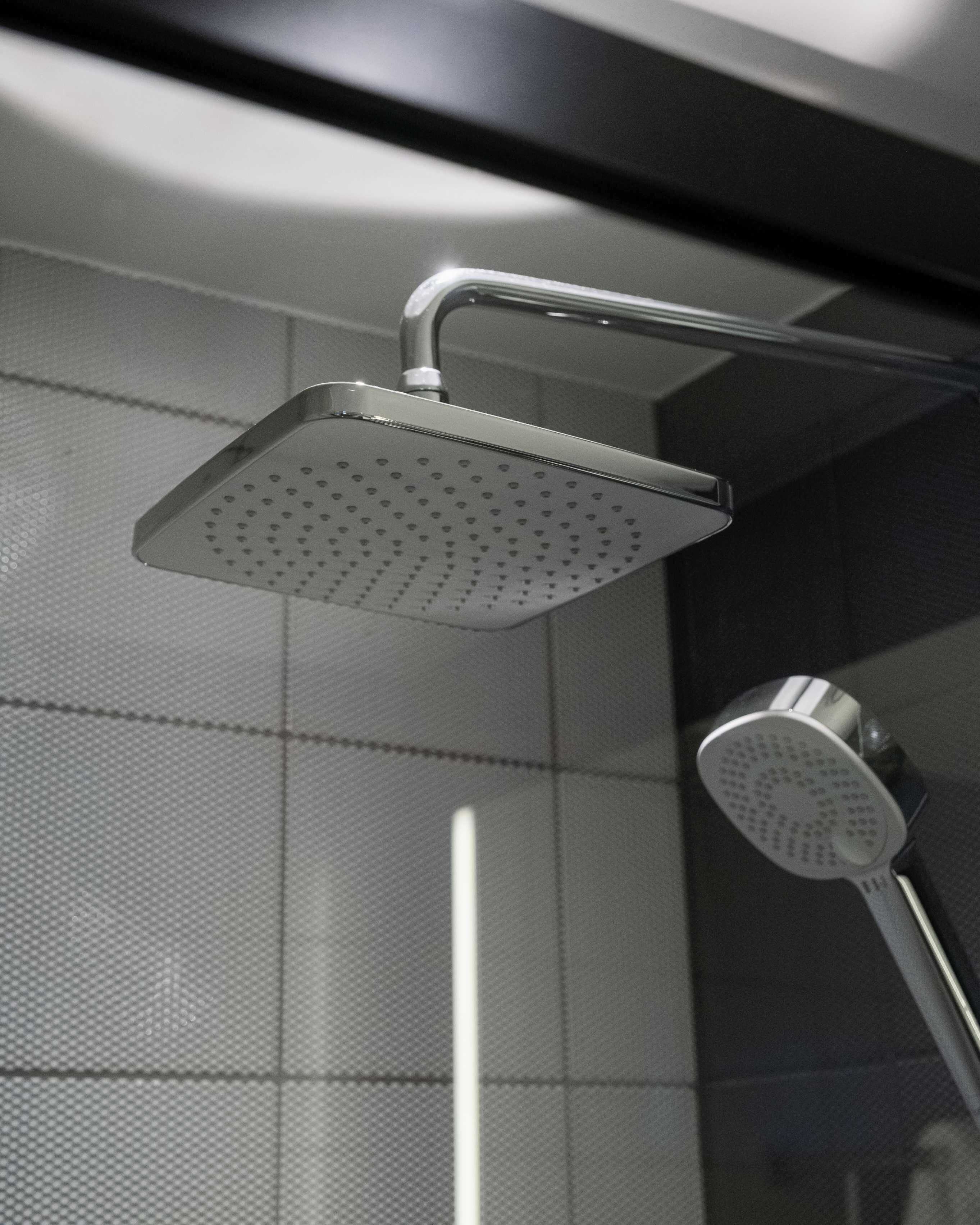 A modern shower with a square, perforated head and a curved handle.