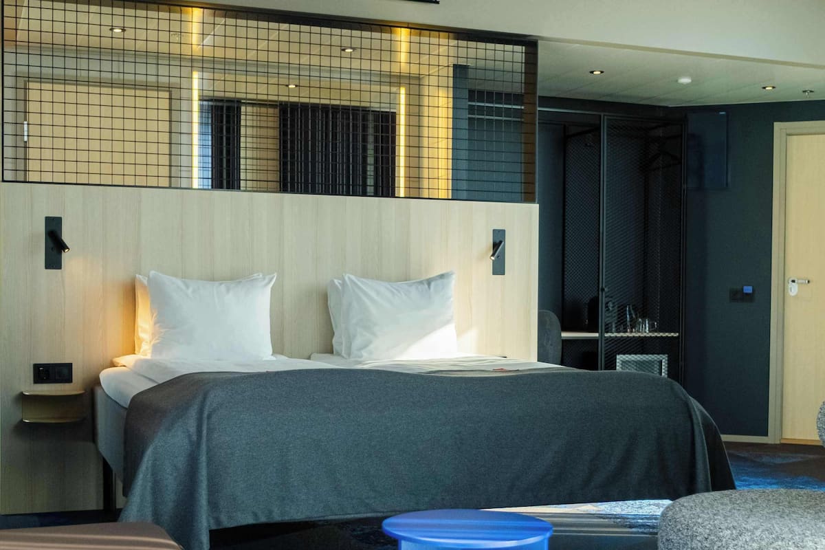 A modern hotel room with a large bed, a small blue stool, and a round table.