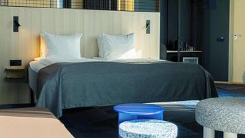 A modern hotel room with a large bed, a small blue stool, and a round table.