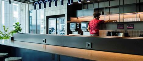 A modern bar area with a counter, seating, and a person working behind the bar.