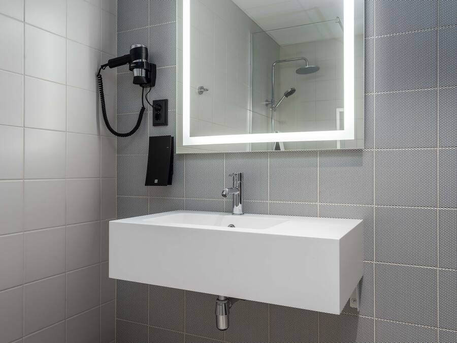 A bathroom with a white sink, a mirror, and a hairdryer mounted on the wall.