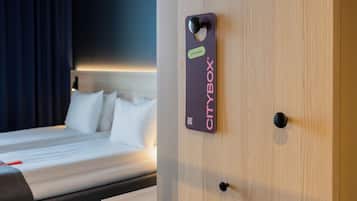 A CityBox® sign on a wooden door, a bed with white linens, and a dark curtain in a hotel room.