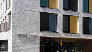 Un edificio moderno con un letrero que dice 'CITYBOX', con fachada de ladrillo y ventanas amplias.