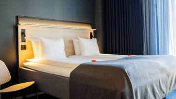 Una habitación de hotel con cama, una silla y ventana con cortinas.