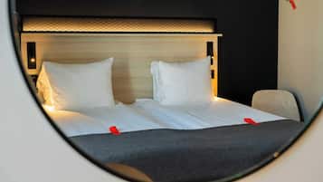 Un letto con lenzuola bianche e due cuscini, una testiera con pannello illuminato e una parziale vista di una sedia.