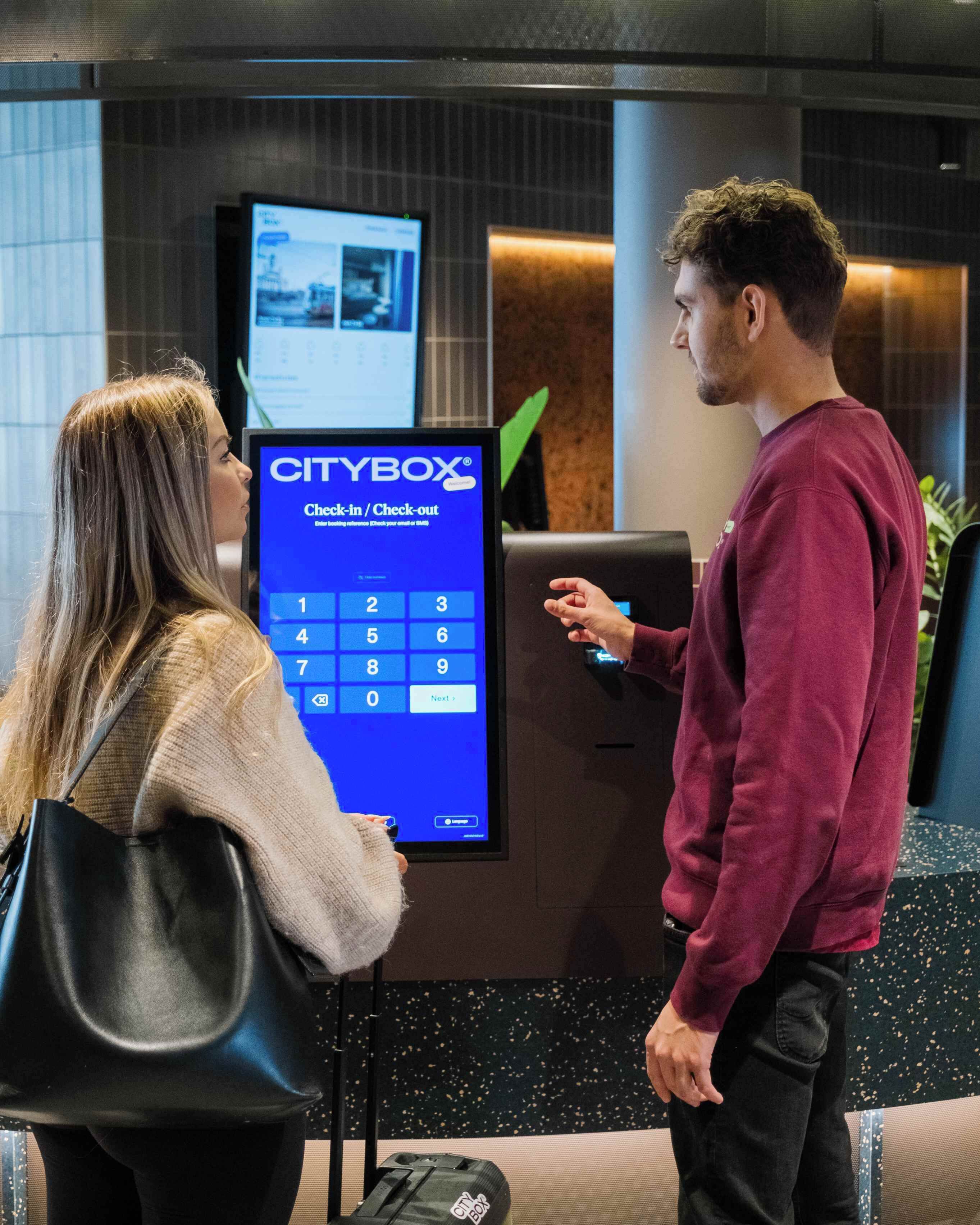 A check-in/check-out kiosk with a digital screen displaying a keypad and a "CITYBOX" logo.