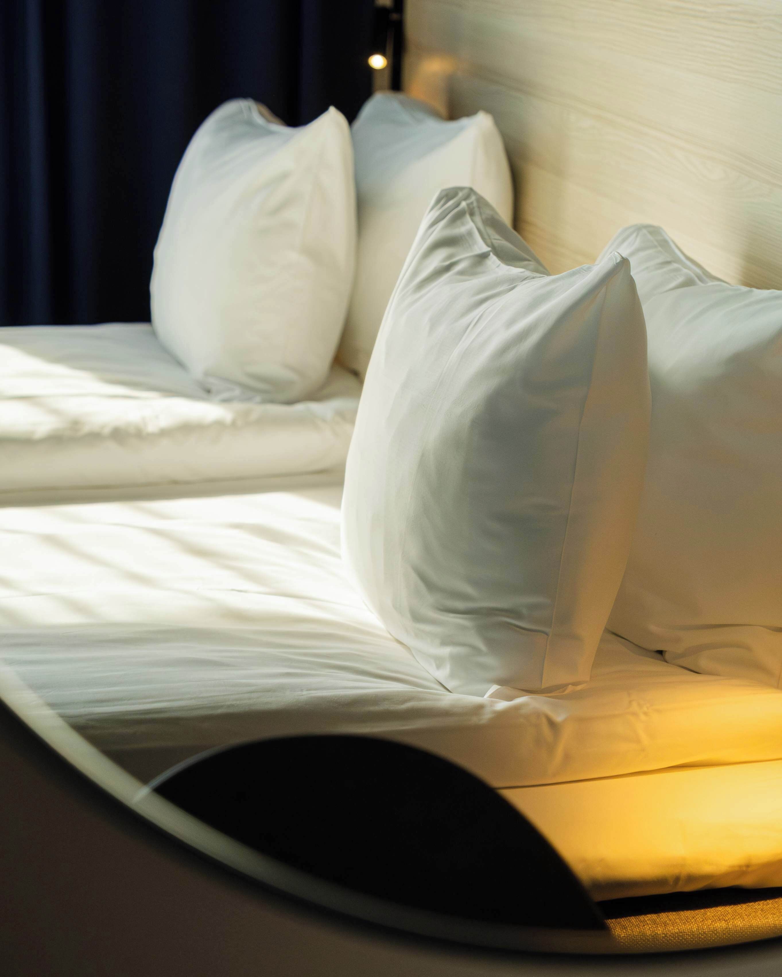 A neatly made bed with white linens and pillows, a headboard, and a bedside lamp.