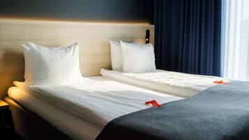 A double bed with white linens and a grey throw blanket, a wooden headboard, and a nightstand with a lamp.