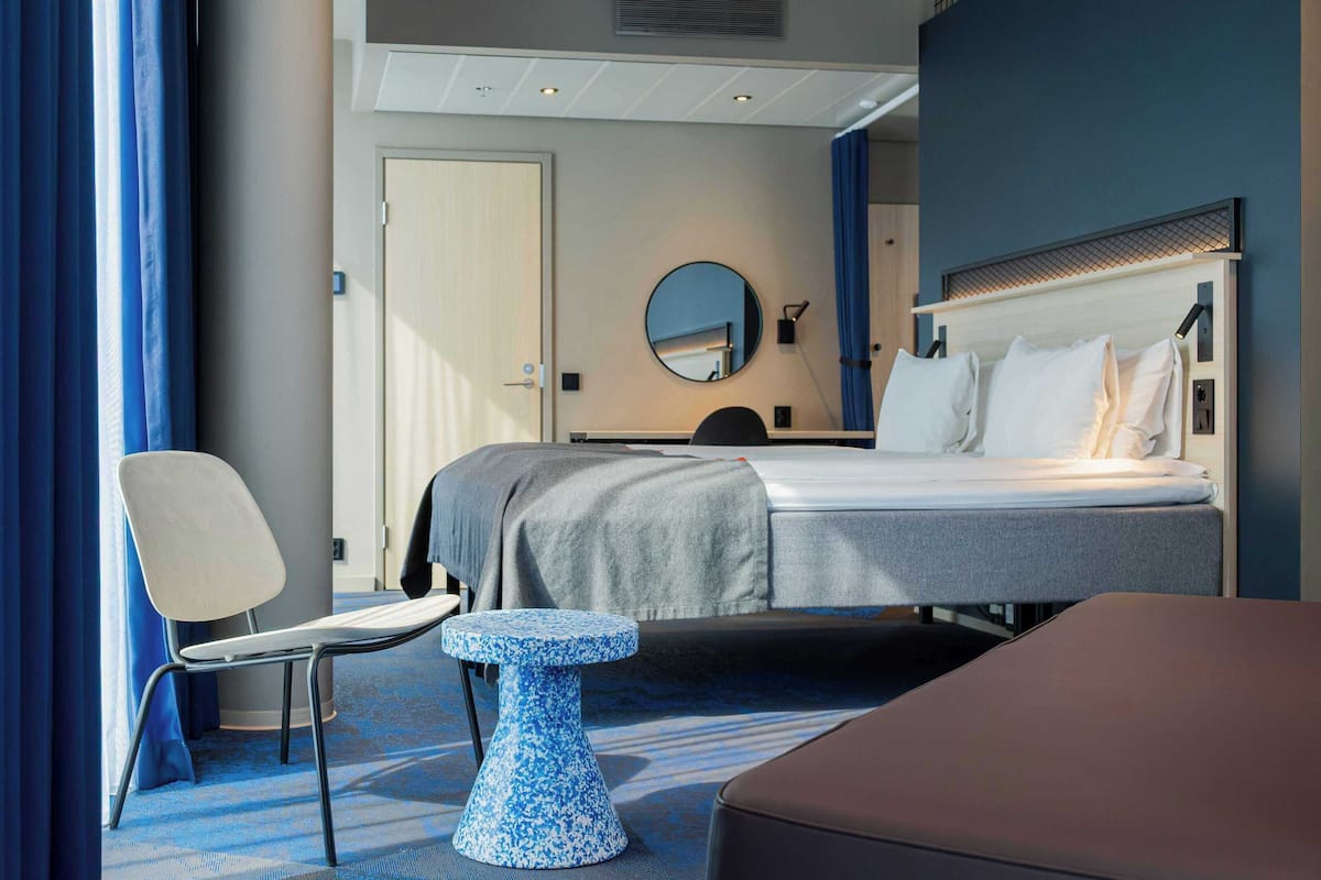 A modern hotel room with a bed, a round mirror, a small table, and a chair.