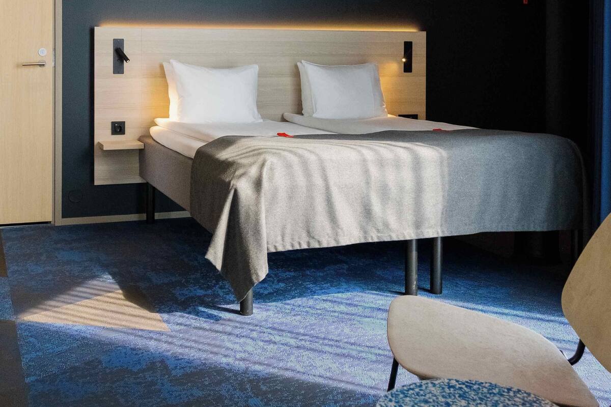 A modern hotel room with a bed, bedside tables, a chair, and a carpeted floor.