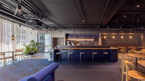 Un bar moderno con taburetes, una barra y una zona de estar con mesas y sillas.