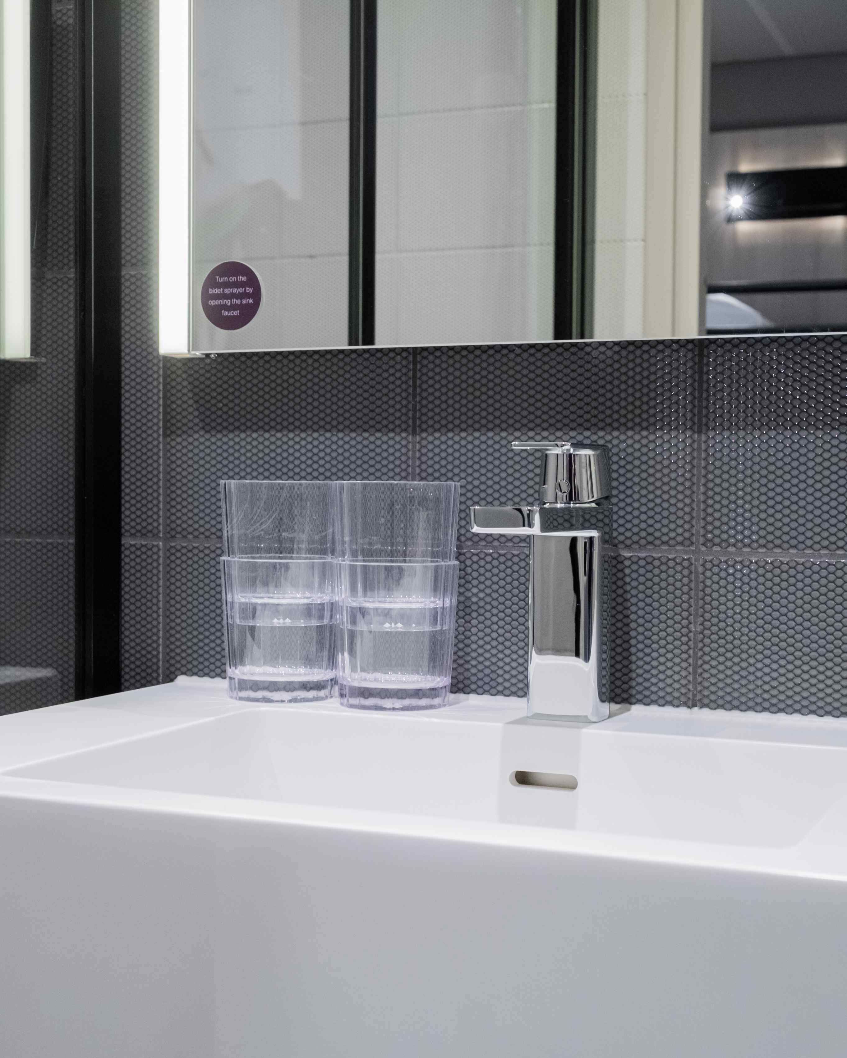 Une salle de bain moderne avec un lavabo blanc, deux verres transparents et un robinet.