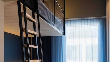 Una habitación de hotel con una cama litera, un escritorio, una silla y un ventanal con cortinas.