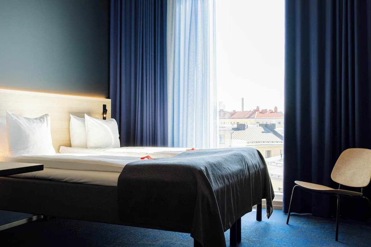 A hotel room with a bed, a chair, and a window with curtains.