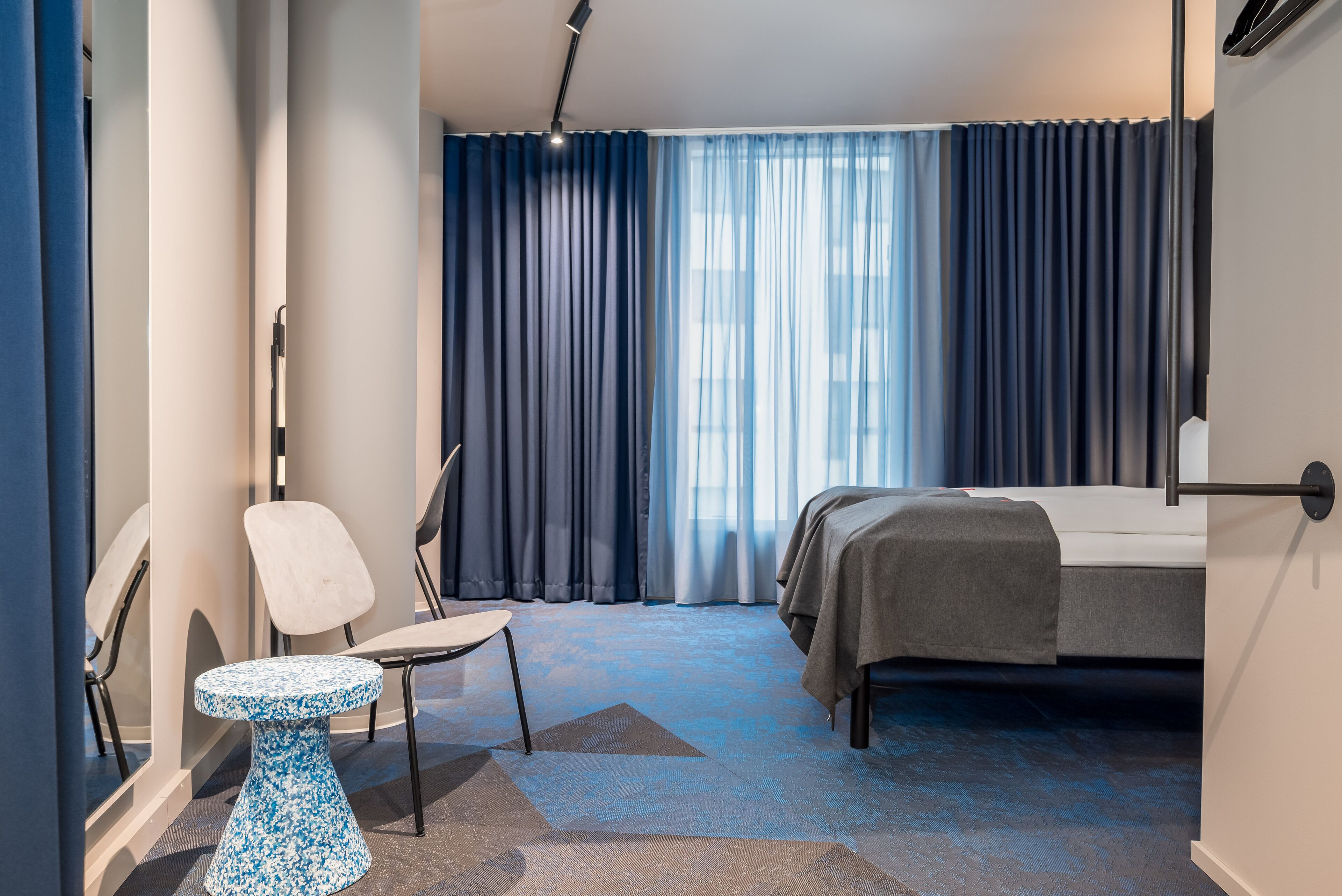 A modern hotel room with a bed, a small round table, a chair, and a large window with curtains.
